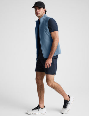 Man wearing a light blue vest over a black shirt on a plain background. 