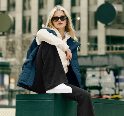 model is wearing a blue puffer jacket, white hoodie, and black high-waisted flare leggings.