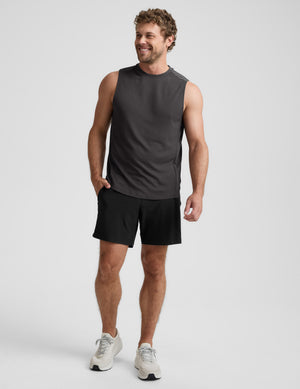 Man wearing a black sleeveless shirt and shorts on a light gray background. 