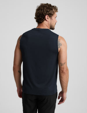 Man wearing a blue sleeveless shirt and black shorts against a light background. 