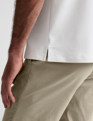 Man wearing a white polo shirt and khaki pants on a plain background. 