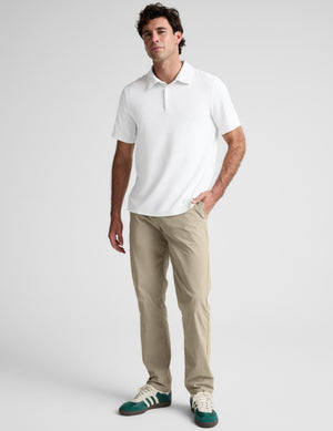 Man wearing a white polo shirt and khaki pants on a plain background. 