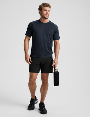 Man wearing a navy t-shirt and black shorts, holding a black water bottle on a light gray background. 