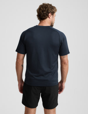 Man wearing a navy athletic shirt and black shorts on a light gray background. 