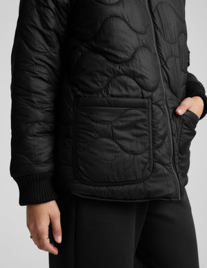 Woman wearing a black quilted jacket on a light gray background. 