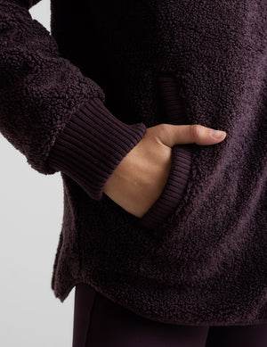 Woman wearing a quilted and boucle purple jacket on a light gray background. 