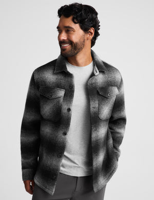 A man wearing a charcoal and black textured overshirt jacket over a light gray t-shirt, photographed against a solid light gray background.