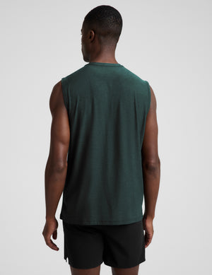 Man wearing a dark green muscle tank top and black shorts against a plain studio background. 