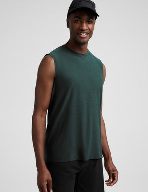 Man wearing a dark green muscle tank top and black shorts against a plain studio background. 