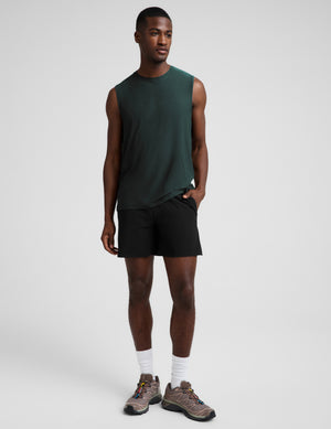Man wearing a dark green muscle tank top and black shorts against a plain studio background. 