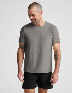 A man wearing a plain gray short-sleeve crewneck t-shirt and black athletic shorts, standing against a light gray studio background.