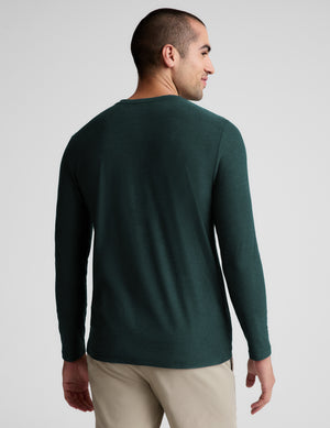 A man wearing a dark green long-sleeve crewneck shirt, shown from a rear three-quarter angle against a light gray studio background.