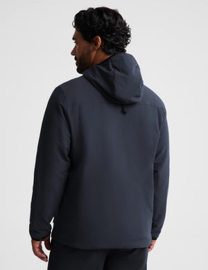 A man wearing a dark navy hooded jacket, shown from the back against a light gray studio background.