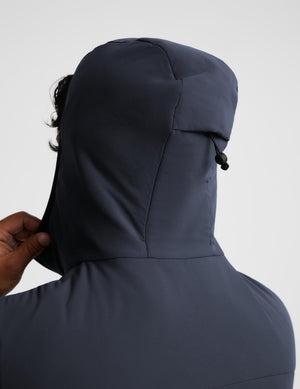 Close-up back view of a person wearing a dark navy hooded jacket, with a hand adjusting the hood against a light gray studio background.
