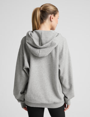 A woman viewed from the back wearing an oversized light gray heather hoodie and black leggings against a plain light gray studio background. | womens