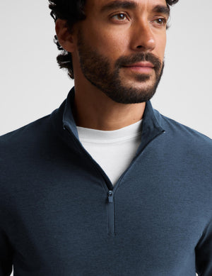 A close-up of a man wearing a navy blue quarter-zip pullover over a white crew-neck t-shirt, photographed against a light gray studio background.