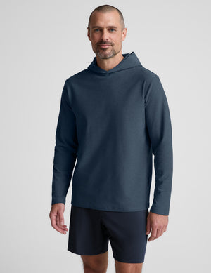 A man wearing a dark slate blue long-sleeve hooded shirt and matching dark shorts, standing against a light gray studio background.