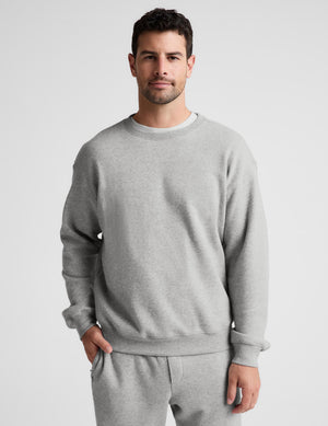 A man wearing a light gray crewneck sweatshirt and matching gray sweatpants, standing against a light gray studio background.