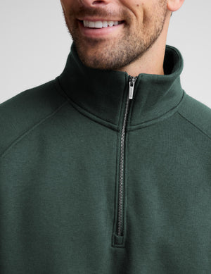 Close-up of a man wearing a dark forest green quarter-zip pullover sweatshirt, showing the collar, zipper, and fabric texture against a light gray background.