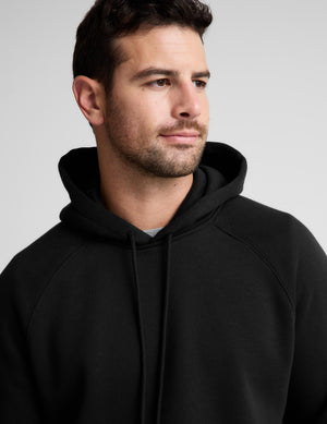 A man wearing a black pullover hoodie with drawstrings, shown in a close-up profile view against a neutral gray background.