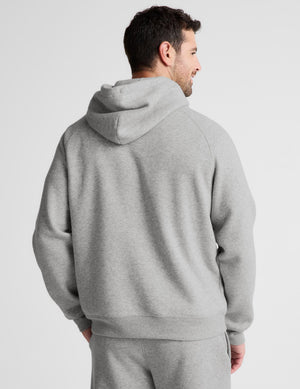 A man wearing a light gray heather pullover hoodie and matching sweatpants, shown from the back against a light gray studio background.