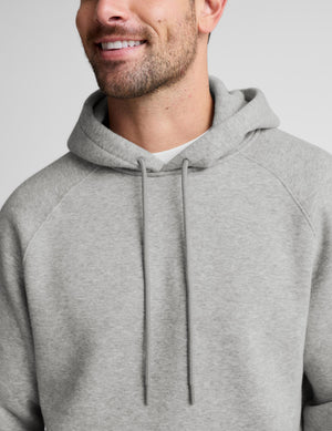 A close-up of a man wearing a light gray heather pullover hoodie with matching drawstrings, shown from the chest up against a plain light gray background.