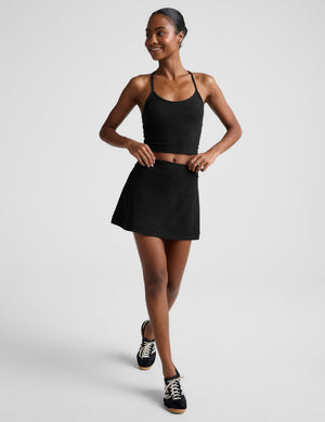 Woman wearing a black tank top and skirt with sneakers on a light gray background. 