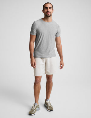Man wearing Cream Beach Washed Terry Men's Short with an elastic waistband, styled with a grey t-shirt and olive sneakers.