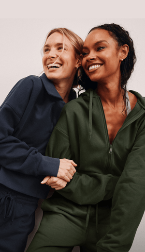 Two women, one in a blue fleece set and one in a green fleece set, posing together against a plain background. 