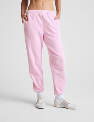 Person wearing pink sweatpants and white sneakers on a light gray background. 