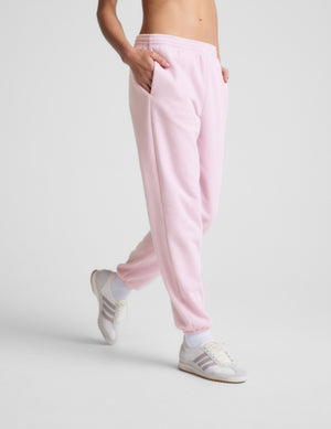 Person wearing light pink sweatpants and white sneakers on a gray background. 