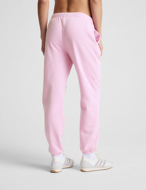 Person wearing pink sweatpants and white sneakers on a light gray background. 