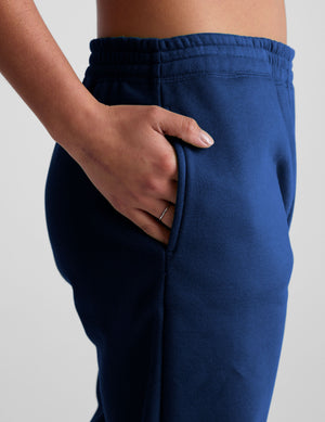 model wearing a blue cropped racerback tank and fleece joggers with pockets on a light gray background.