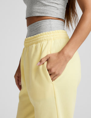 Woman wearing a gray tank top and yellow sweatpants on a plain background. 