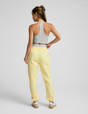 Woman wearing a gray tank top and yellow sweatpants on a plain background. 