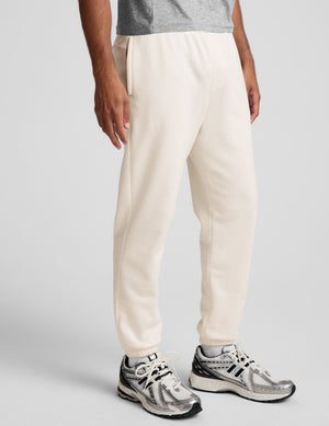 man wearing a gray crew neck t-shirt and white fleece sweatpants on a plain background. 