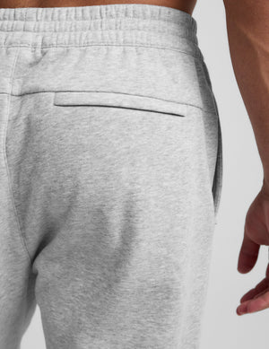 man wearing a black crew neck t-shirt and gray fleece sweatpants on a light gray background. 