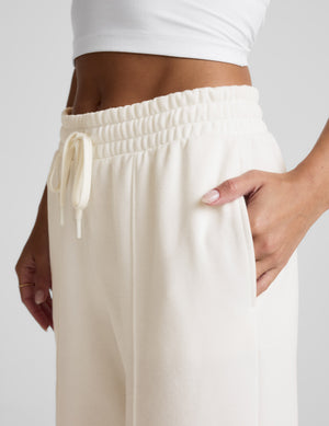 Woman wearing a white fleece sweatshirt and pants with a plain background. 