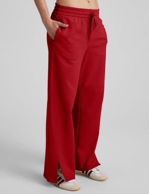 woman wearing a red fleece pants with side slits against a plain background. 