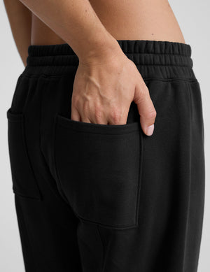model is wearing black fleece barrel style sweatpants against a plain background. 
