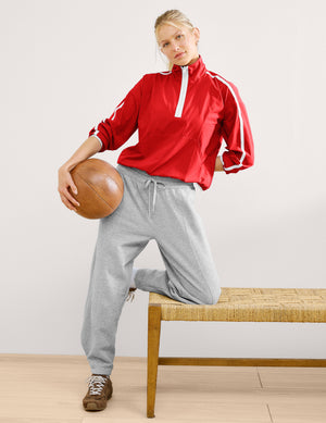 Woman wearing a red jacket and grey sweatpants against a plain background. 