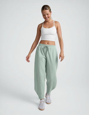 Smiling woman in sage green LuxeFleece Barrel Sweatpants with drawstring waist and barrel leg silhouette, walking forward.