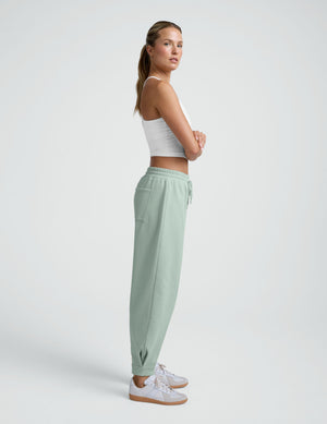 Side view of a model in sage green LuxeFleece Barrel Sweatpants with a tapered leg, elastic waist, and ankle pleat detail.