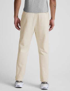 man wearing a cream-colored straight leg fleece sweatpants on a plain background. 