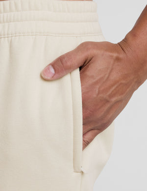 man wearing a cream-colored straight leg fleece sweatpants on a plain background. 