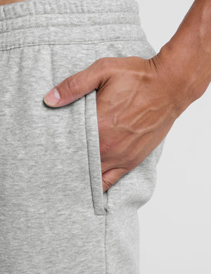 man wearing a gray straight leg fleece sweatpants on a plain background. 