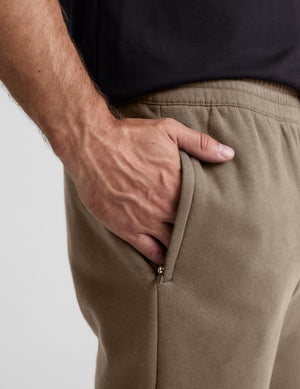 Man wearing brown sweatpants on a light gray background. 