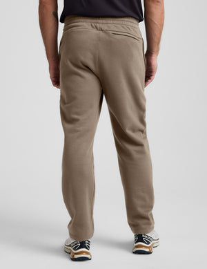 Man wearing brown sweatpants on a light gray background. 