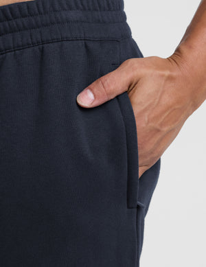 man wearing navy blue straight leg fleece sweatpants on a plain background. 