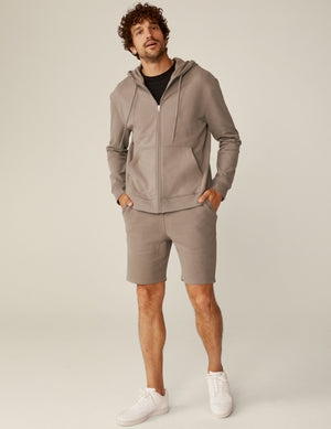 model is wearing a brown men's zip-up hooded jacket.
